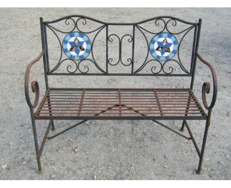 A weathered tubular steel framed two seat garden bench with strapwork seat, open scrolled arms and back with circular mosaic 