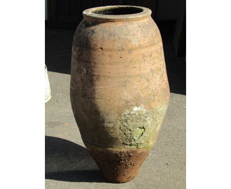 A weathered terracotta oviform jar with simple incised banded detail, 83cm high