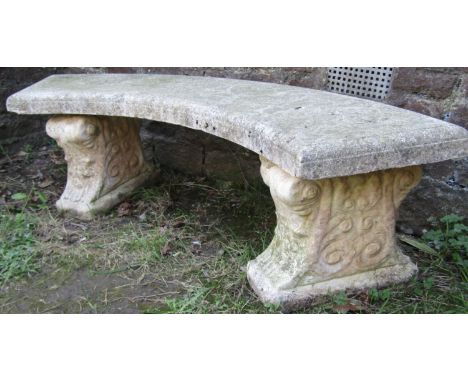 A weathered cast composition stone three sectional garden bench, with crescent shaped seat and acanthus moulded supports, 42c