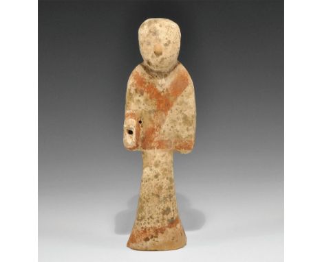 Han Dynasty, 206 BC-220 AD. A hollow ceramic figurine of a standing attendant in a long coat, the right hand raised; red pigm