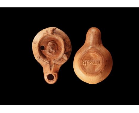 1st-3rd century AD. A pottery oil lamp with comic actor's mask in the indented oil chamber, lugs to the edge and long nozzle;