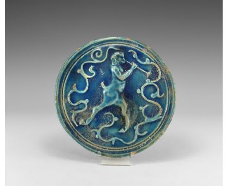 17th-19th century AD. A blue-glazed ceramic plaque with recessed border, high-relief profile image of an advancing faun blowi
