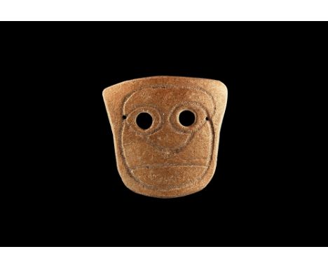 4th-3rd century BC. A heater-shaped slightly curved ceramic mask with two eye-holes and incised stylised facial details; pier