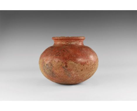 1st millennium BC. A squat ceramic jar with waisted neck and rolled rim, red glaze with black painted geometric band to the s