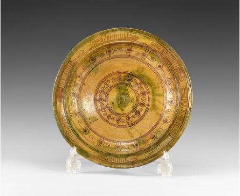 12th-14th century AD.
A ceramic dish with mottled green and ochre glaze, basal ring, carinated with flat outer edge to the ri