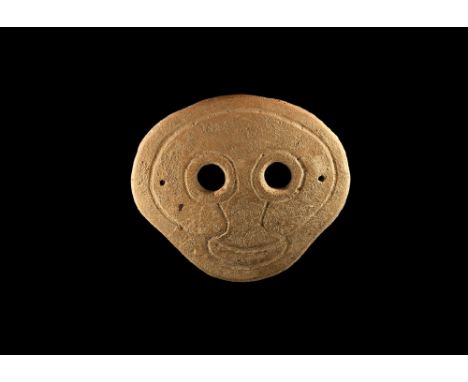 4th-3rd century BC. A discoid slightly curved ceramic mask with two eye-holes and incised stylised facial details; pierced at