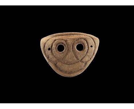 4th-3rd century BC. A D-shaped slightly curved ceramic mask with two eye-holes and incised stylised facial details; pierced a