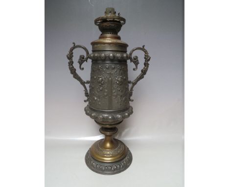 A TALL TWIN HANDED URN SHAPED OIL LAMP, the bronzed metal body with fine embossed detail illustrating female figurines, with 