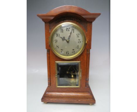 AN OAK CASED EDWARDIAN TORSION CLOCK, having a silvered dial, later filigree hands, and bevelled glass door exposing a brass 