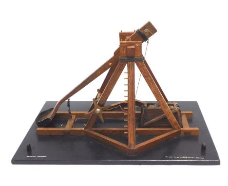 A model of a Medieval Trebuchet or siege engine, possibly in oak, on an ebonised base, 43cm wide, with red painted travelling