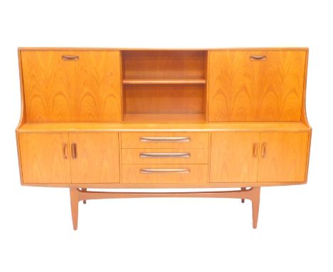 A 1970's teak sideboard, the raised top with a two fall-front doors, flanking a shelf the base with arrangement of three draw