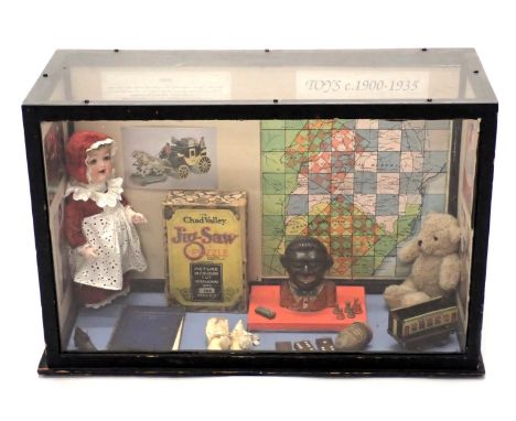 A display case showing toys from 1900-1935, to include a money box*, jigsaw, etc., 64cm wide.In compliance with the-saleroom.