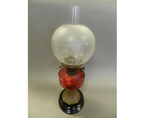 A brass and glass oil lamp, circa 1900, with cranberry reservoir, the globe acid etched with stylised foliate forms