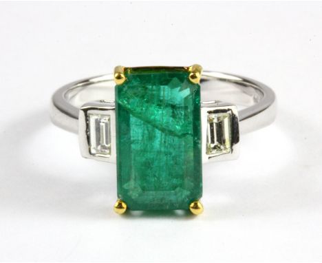 An 18ct white gold (stamped 750) ring set with a 3ct emerald cut emerald and baguette cud diamond set shoulders, (N).