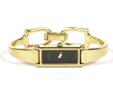 A ladies gold plated Gucci quartz bangle watch, black dial, signed Gucci, with a tapering stiff bangle terminating in a horse