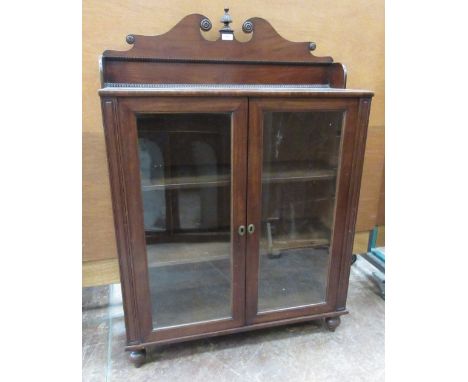 A Regency mahogany Cabinet with low raised back having swan neck surmount and carved finial above pair of plain glazed doors 