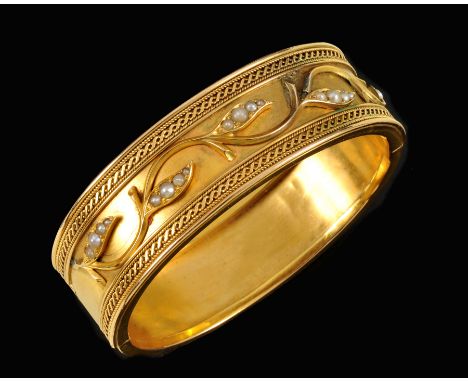 A Victorian hinged Bangle the front with applied foliate design set graduated seed pearls between wirework borders, tests as 