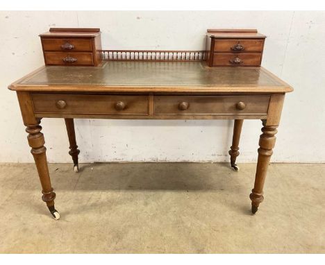 A leather topped writing desk with two main drawers on turned legs and large ceramic castors, galleried top with four small d