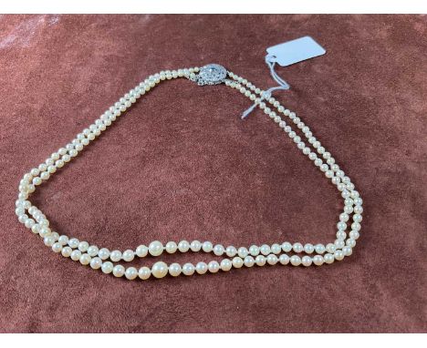 A two strand graduated cultured pearl necklace, set with a 9ct white gold pierced circular clasp centred with a sapphire, len