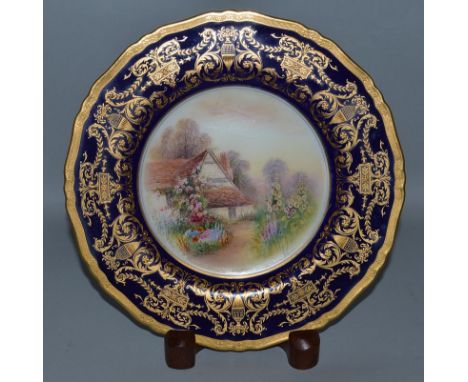A ROYAL WORCESTER PLATE painted with a thatched Cottage by RAYMOND RUSHTON, signed under a blue and neo-classical gilt border