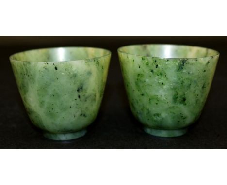 A PAIR OF CHINESE JADE CUPS, the predominantly green stone with darker and lighter inclusions, each 2.9in diameter & 2.4in hi