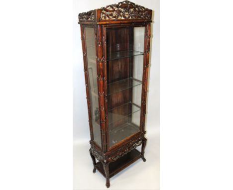 A GOOD CHINESE REDWOOD STANDING DISPLAY CABINET, the frieze carved with fruiting vine over a long glass fronted door, glass s