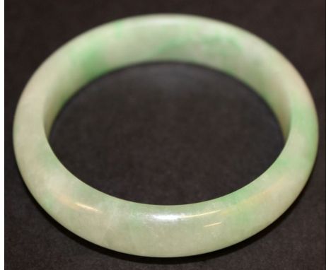 A CHINESE JADEITE BANGLE, the whitish stone with apple-green inclusions, 2.8in diameter, the inner rim 2.2in diameter.