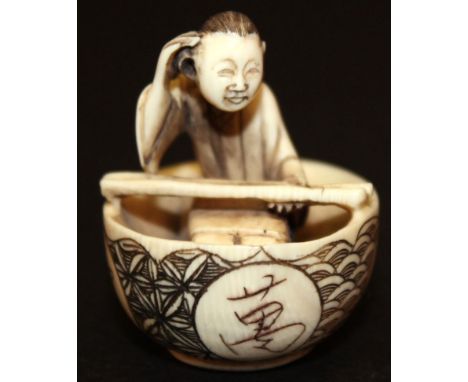 A GOOD QUALITY SIGNED JAPANESE IVORY NETSUKE, of a kneeling man in a basket-form boat engraved with character roundels on a w