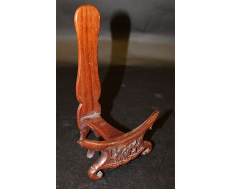 AN EARLY 20TH CENTURY CHINESE CARVED HARDWOOD PLATE STAND, supported on scroll feet and carved to the front with a foliate sp