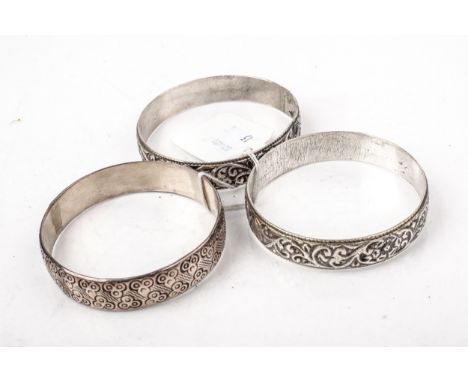 A silver broad slave bangle and two white metal examples. The first deeply engraved with circle-trefoils, Birmingham 2000, 63