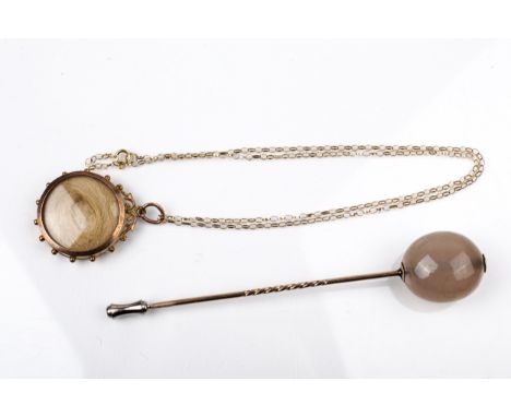 An early 20th century gold double-sided locket and an agate bead stick pin. The locket with a beaded border, applied oval pan