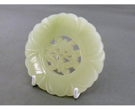 A Chinese pale celadon jade circular plaque, finely carved in the form of lotus and pierced in the centre with a pair of butt