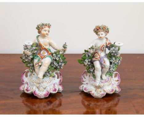 A pair of 18th century Derby porcelain candlestick figures, each in the form of a seated partly draped cherub with floral wre