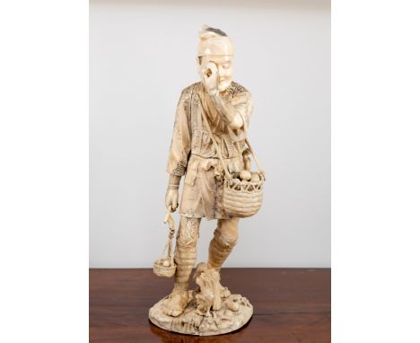 A large Japanese sectional carved ivory figure of an egg tester, Meiji period (1868-1912), holding an egg to his eye, a baske