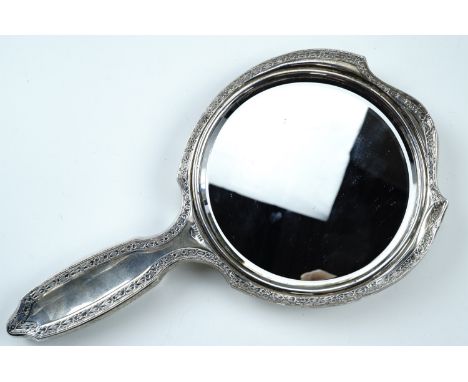 An early 20th Century silver hand mirror, of shield shape with a round bevelled mirror and having an Aesthetic influenced bor