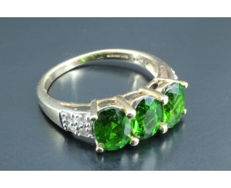 A lady's three stone dress ring, having three green oval stones approximately 4.5 x 7 mm, in a 9 carat gold triple basket set