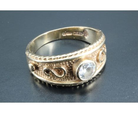 An unusual solitaire ring, being a 9 carat gold textured tapering broad band, with rope and bead border and a central bezel s