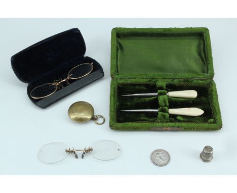 A brass sovereign case with a 1911 1 frank coin, two pairs of vintage spectacles, cased picks, and a thimble