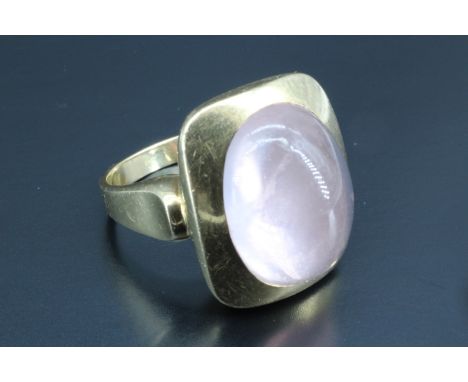 A 1970s rose quartz cabochon finger ring, having a 15 x 11 mm, oval cabochon, bezel set in an oblong gold cushion, 20 x 16 mm