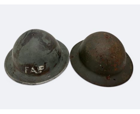 Two WWII Home Front helmets. A First Aid Party non-magnetic helmet missing strap and liner, and a magnetic Home Front helmet 