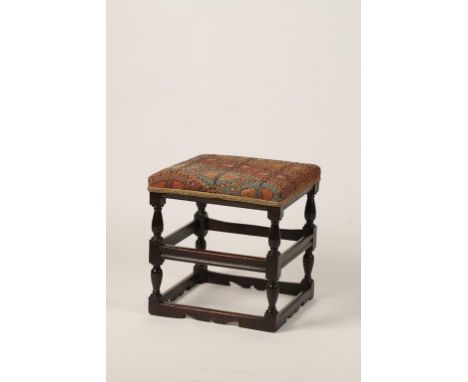 A CHARLES II WALNUT STOOL with a padded square seat on turned legs united by moulded square stretchers with cut-out decoratio