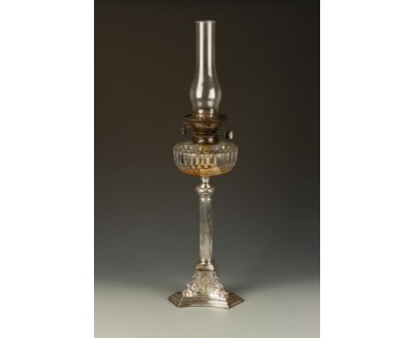 AN EDWARDIAN SILVER MOUNTED OIL LAMP with a cut-glass circular reservoir, cylindrical shade above a corinthian style column, 