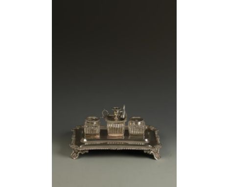 A GEORGE IV INK STAND of shaped rectangular form with gadrooned and scroll borders, the centre with a detachable chamberstick