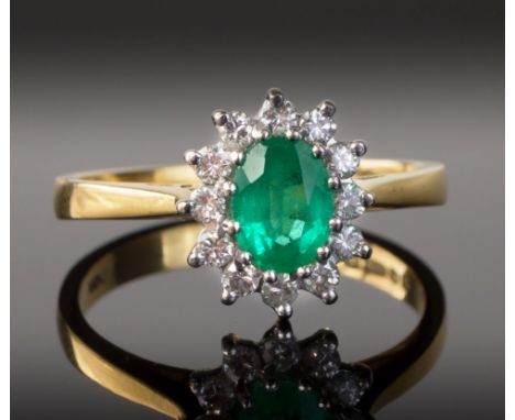 An 18ct yellow gold, emerald and diamond cluster ring, the oval cut emerald within a border of brilliant cut diamonds, ring s