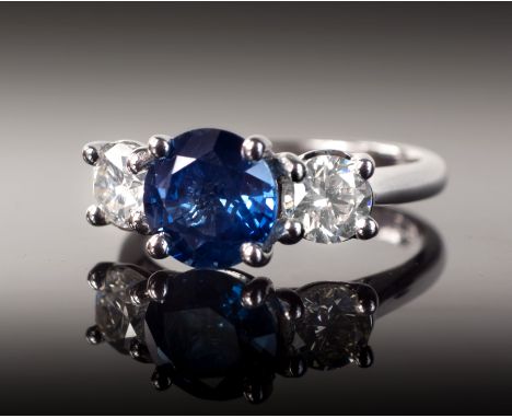 An 18ct white gold, sapphire and diamond three stone ring, the central 2.42ct round cut sapphire of fine colour, flanked by t