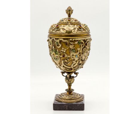 A 19th century Continental gilt bronze covered urn, decorated with glass jewels, masks and wasps, standing on a marble plinth