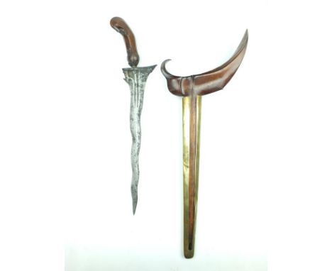 A Kris, 31.5cm wavy watered steel blade, characteristic carved wooden hilt, contained in its brass mounted wooden scabbard.