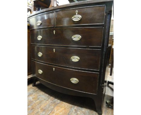 An early 19th century bow fronted bedroom chest with cross banded top over three long and two short graduated drawers with ki