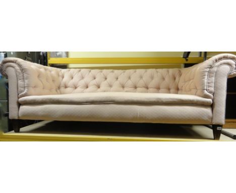 A late Victorian/Edwardian three seat chesterfield sofa, with light pink upholstery, button back and moulded arms raised on s