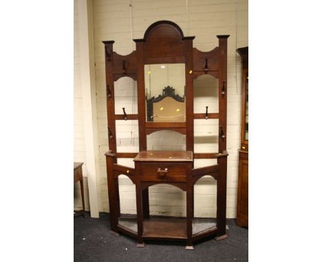 In the manner of Liberty and Co, an oak hallstand, with arched pediment over a bevelled mirror flanked by wooden pegs, glove 